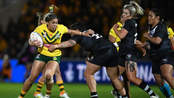 An Australian rugby league player grimaces as she tries to fend off the tackle of a New Zealand defender.