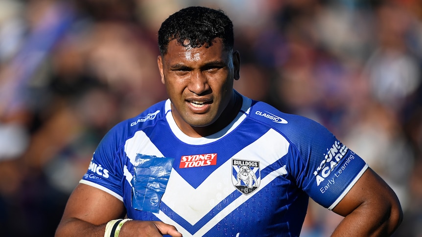 An NRL player stands on the field staring into the sun, getting his breath back during a game.