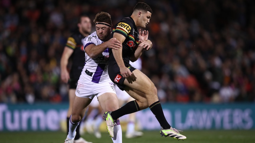 A Penrith Panthers NRL player is tackled by a Melbourne Storm opponent.