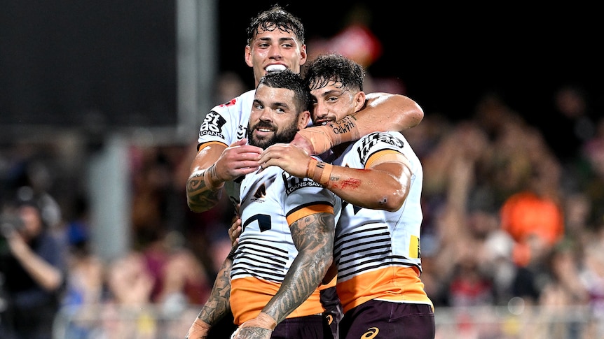 Three Brisbane Broncos NRL players embrace as they celebrate a try.