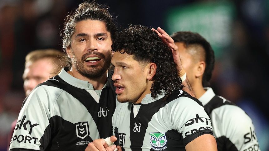 A Warriors NRL player holds the ball as he is congratulated by a teammate after scoring a try against Manly.