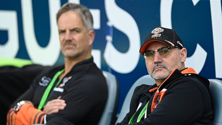 Justin Pascoe and Lee Hagipantelis sit on the sidelines at a Wests Tigers game.