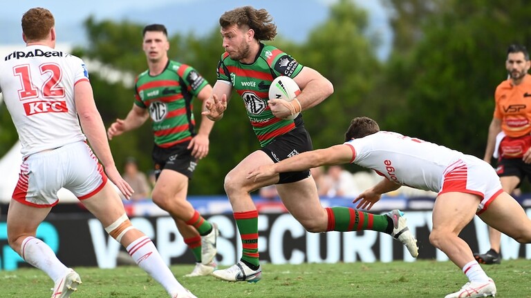 A South Sydney NRL player runs through the middle of the ground with his hair flying behind him..