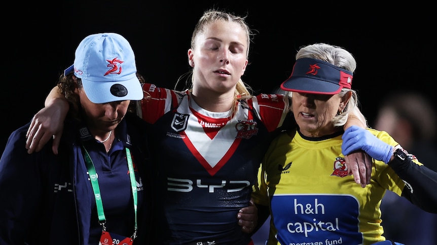 Tarryn Aiken is helped from the field with a knee injury by two Sydney Roosters trainers during an NRLW game.
