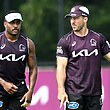 Two Brisbane Broncos players stand next to each other at training as the one on the right looks at his partner.