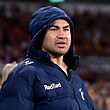 A Melbourne Storm player stands on the sidelines wearing a jacket with a hood on.