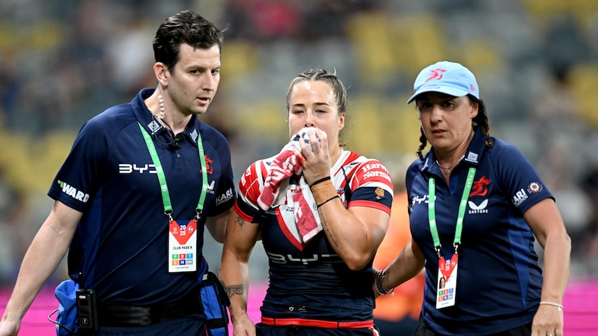 Isabelle Kelly holds a towel to her mouth after an injury in a Sydney Roosters NRLW game.