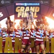 Wigan Warriors' women's team lift the 2025 Super League Trophy, with the word 'CHAMPIONS' in gold letters in front of them